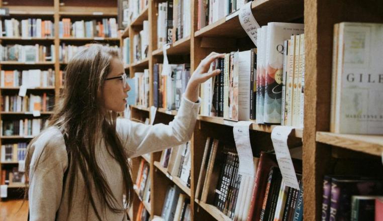 Studentin nimmt ein Buch aus dem Bibliotheksregal.